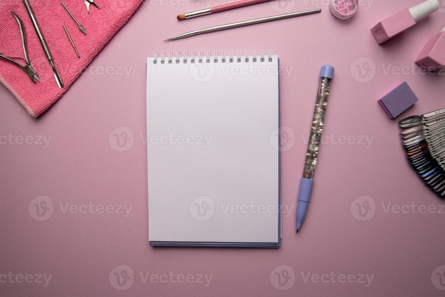 Top view of open empty spiral notebook with pen and manicure accessories on pink background photo