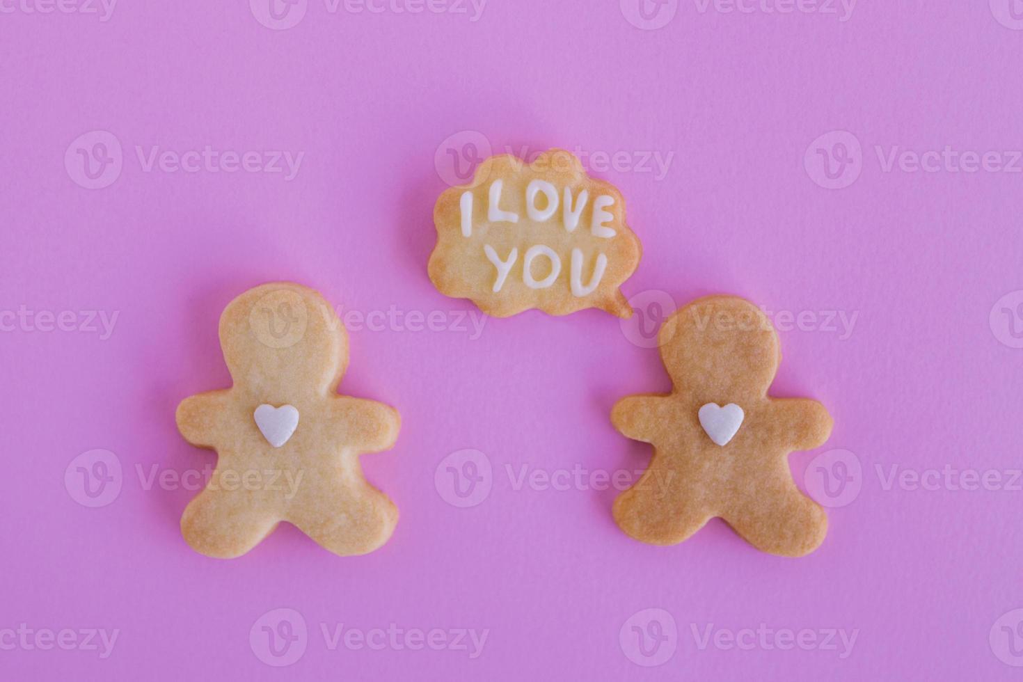 Homemade shortbread cookies with white glaze on pink background, top view. Two people with callout cloud with text - I love you photo