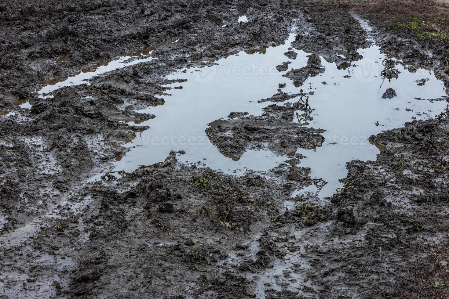 A broken rural country road after the rain. Puddles after rain on a dirt road. Clay, soil and puddles at cloudy day light after rain, autumn season. photo