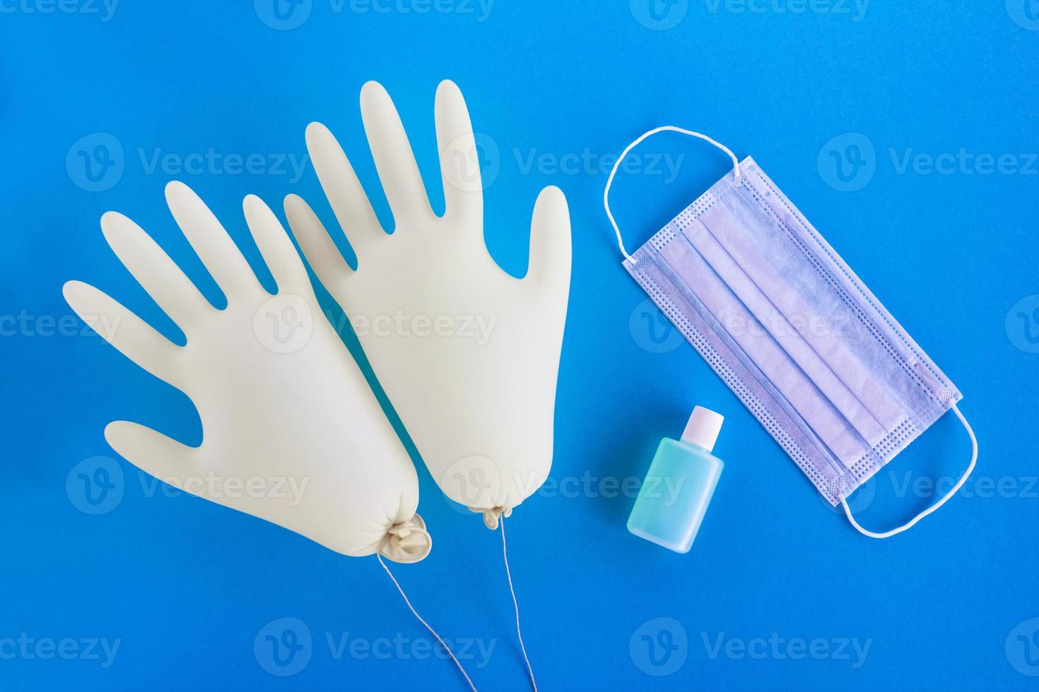 Pair of disposable medical gloves, face mask and hand sanitizer on blue background with copy space. Concept of new normal lifestyle. photo