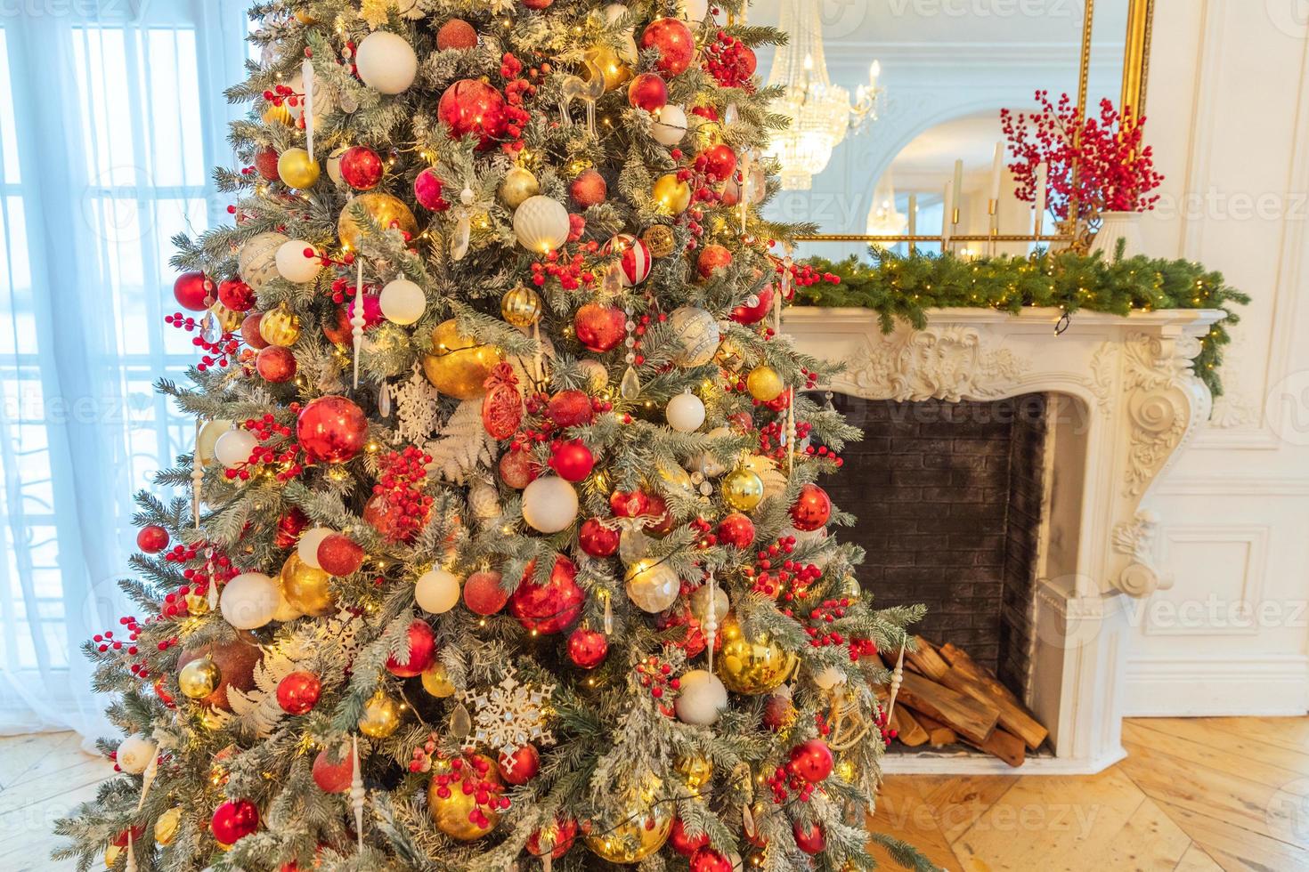 habitación interior clásica decorada en navidad, árbol de año nuevo con adornos rojos y dorados. moderno apartamento de diseño de interiores de estilo clásico blanco con chimenea y árbol de navidad. Nochebuena en casa. foto