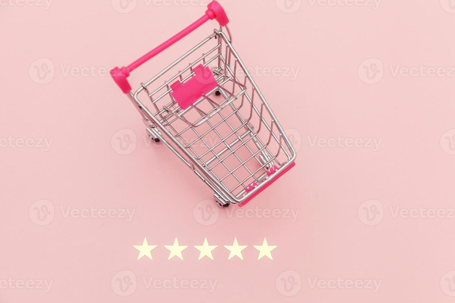 Small supermarket grocery push cart for shopping toy with wheels and 5 stars rating isolated on pastel pink background. Retail consumer buying online assessment and review concept. photo