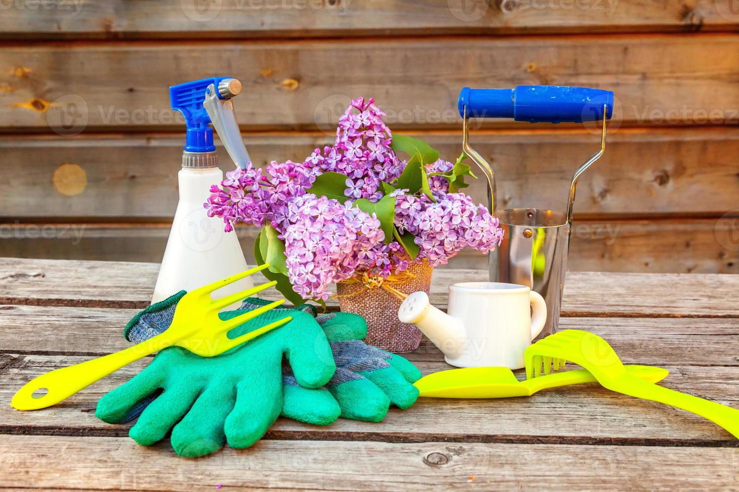 Gardening tools, watering can, shovel, spade, pruner, rake, glove, lilac flowers on vintage wooden table. Spring or summer in the garden, eco, nature, horticulture hobby concept background. photo