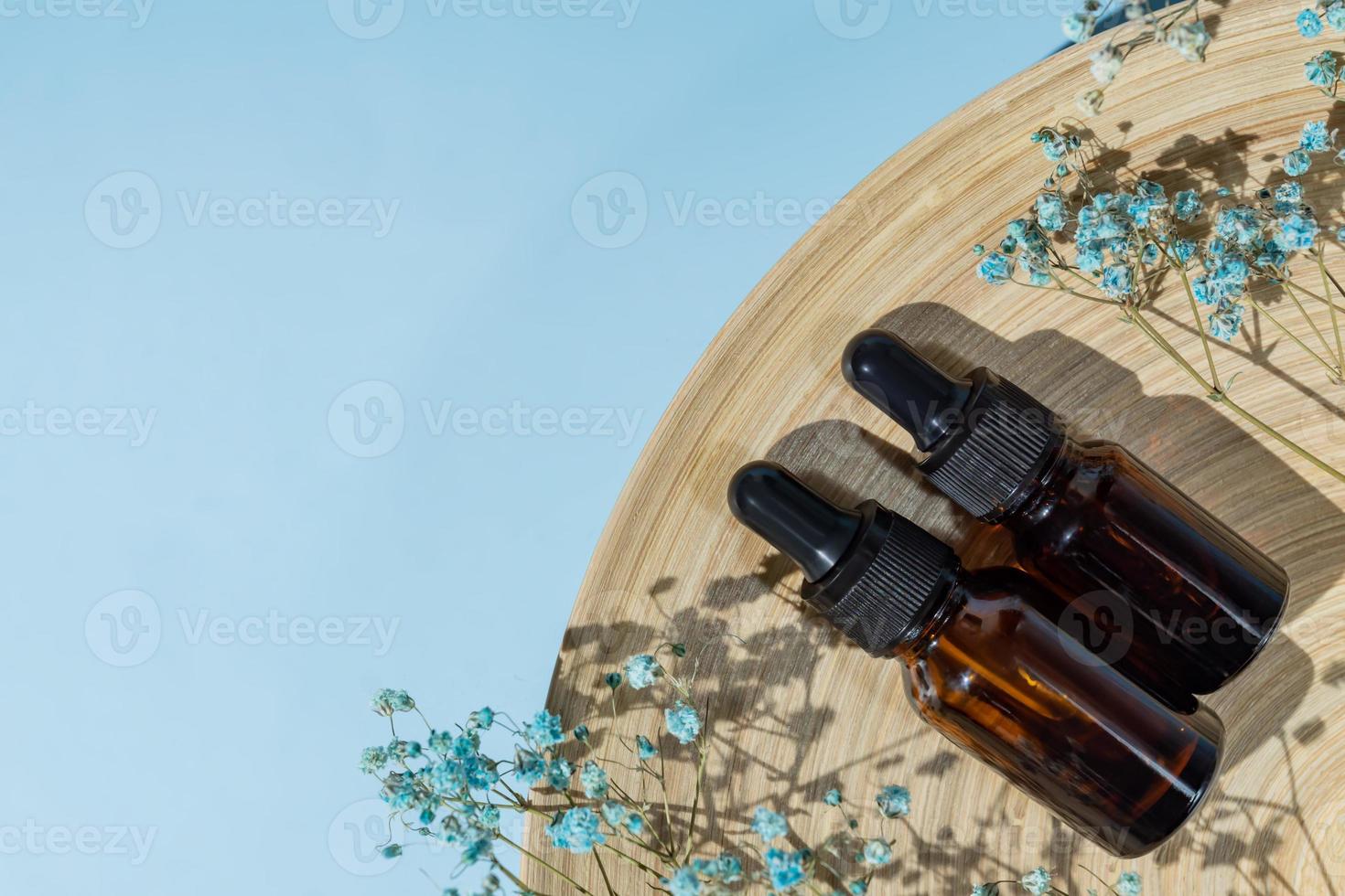 Set of two dark glass dropper bottles with beauty serum or essential oil on bamboo plate decorated with gypsophila flowers on blue background with copy space photo
