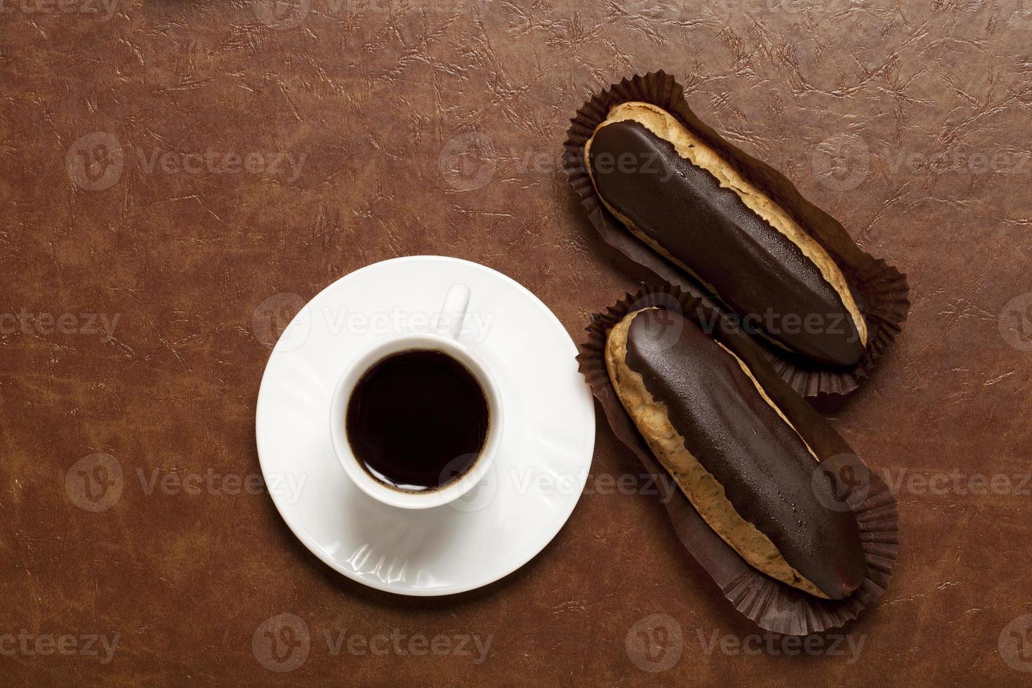 café, eclair de chocolate, café en una taza blanca, plato blanco, sobre una mesa marrón, eclair en soporte de papel foto