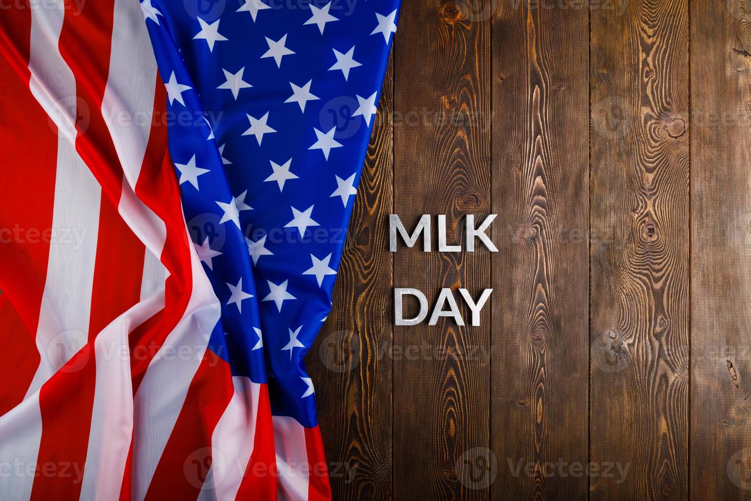 la palabra mlk day colocada con letras de metal plateado sobre una superficie de madera con una bandera de estados unidos arrugada en el lado izquierdo foto