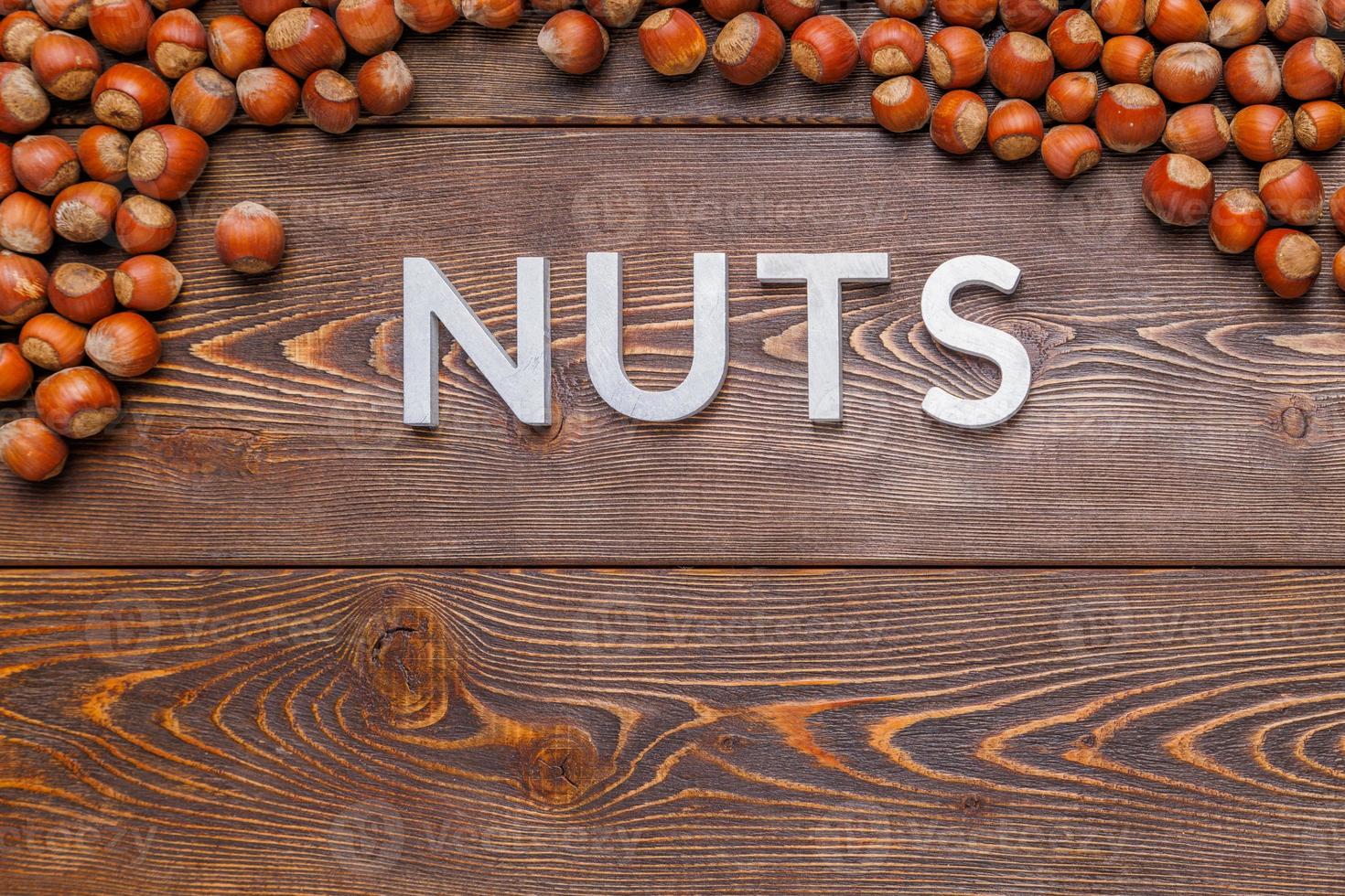 la palabra nueces colocada con letras plateadas sobre fondo de tablero de madera rodeada de avellanas foto