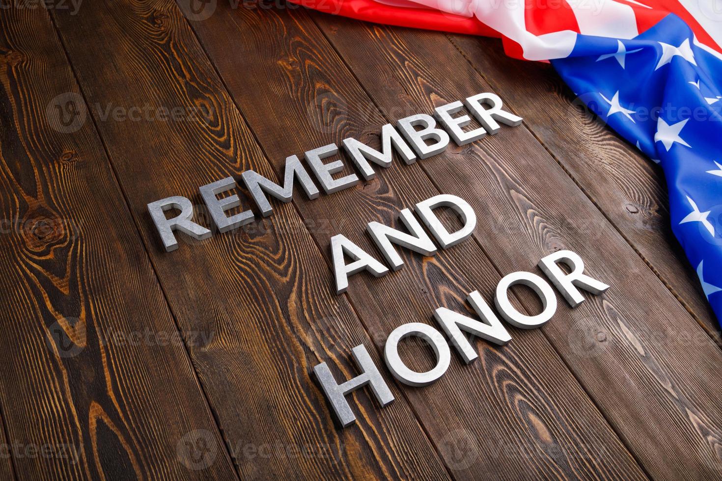 las palabras recuerdan y honran colocadas con letras de metal plateado sobre fondo de madera con la bandera de EE.UU. en el lado derecho foto