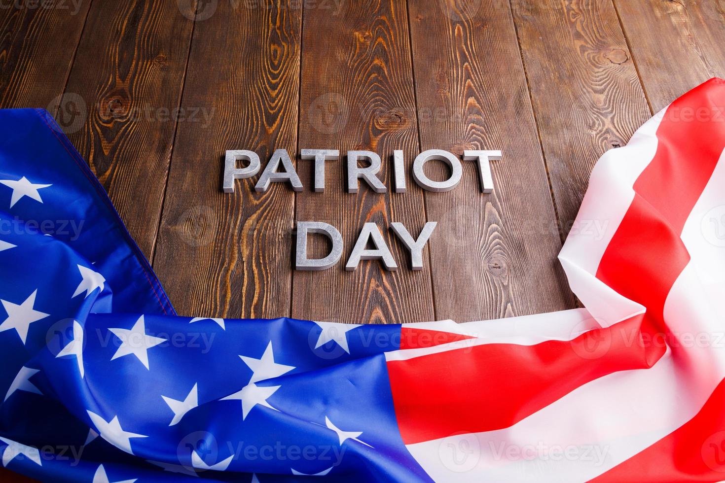 the words patriot day laid with silver metal letters on wooden board surface with crumpled usa flag photo