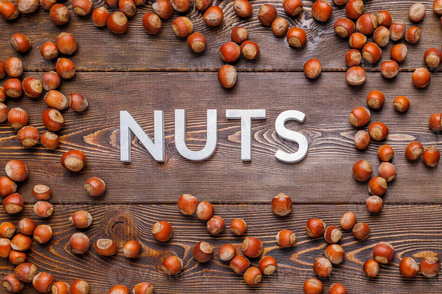 the word nuts laid with silver letters on wooden board background surrounded with scattered hazelnuts photo