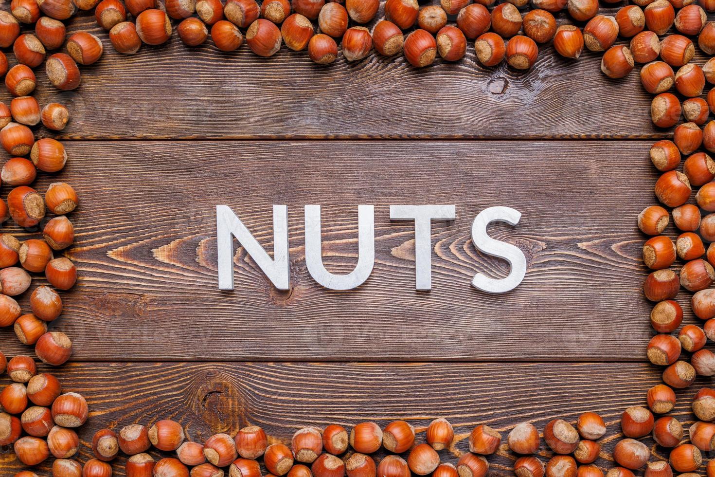 rectangular frame of many hazelnuts with shells on brown wooden surface with word nuts laid with silver letters photo