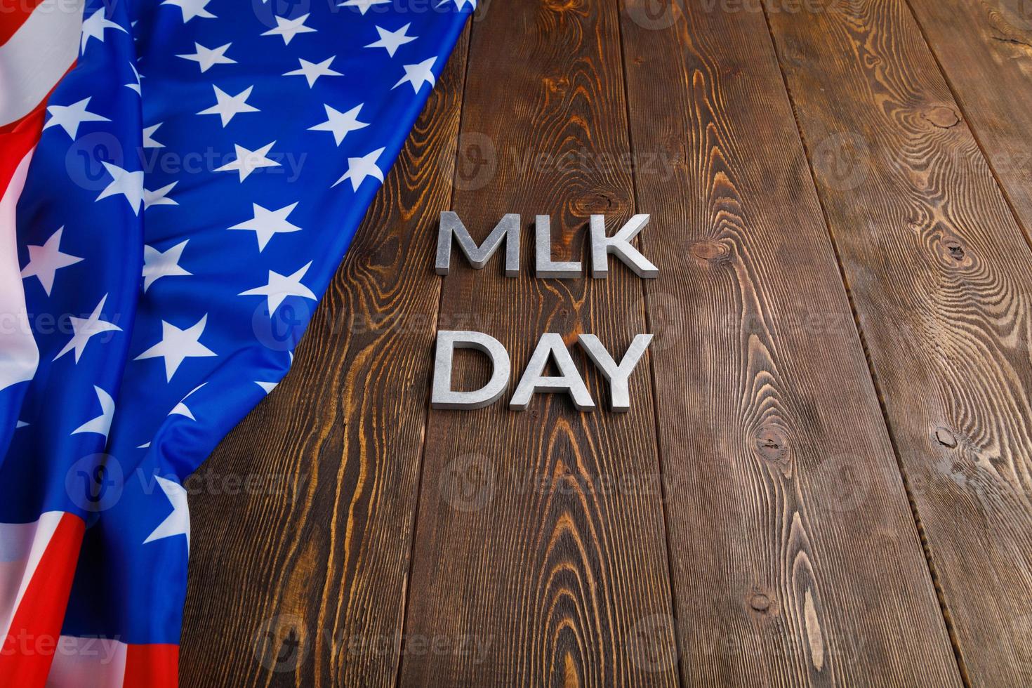 la palabra mlk day colocada con letras de metal plateado sobre una superficie de madera con una bandera de estados unidos arrugada en el lado izquierdo foto