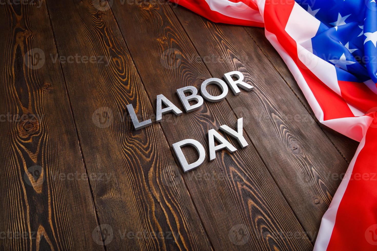 words labor day laid with silver metal letters on wooden surface with crumpled USA flag on left side photo