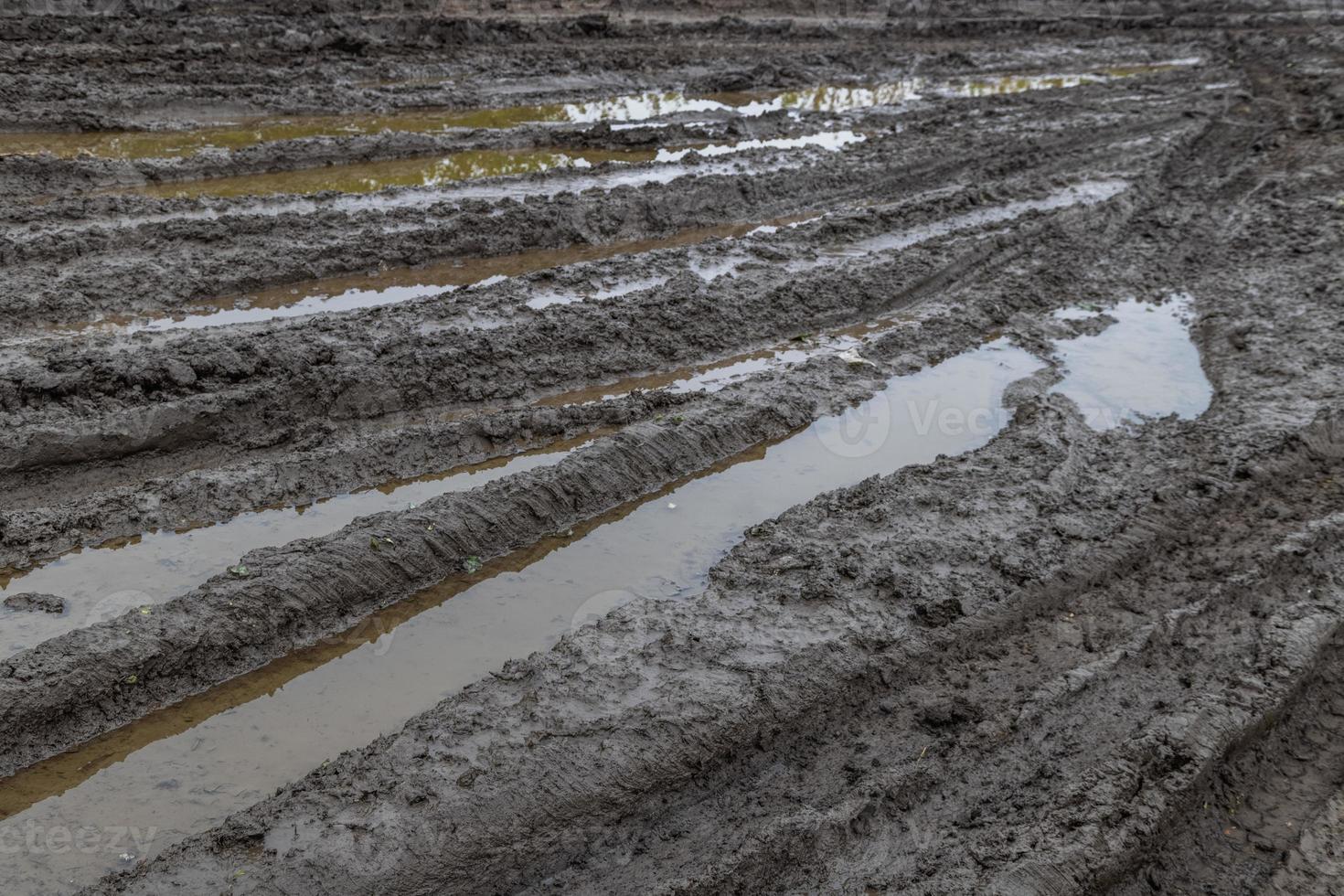 A broken rural country road after the rain. Puddles after rain on a dirt road. Clay, soil and puddles at cloudy day light after rain, autumn season. photo