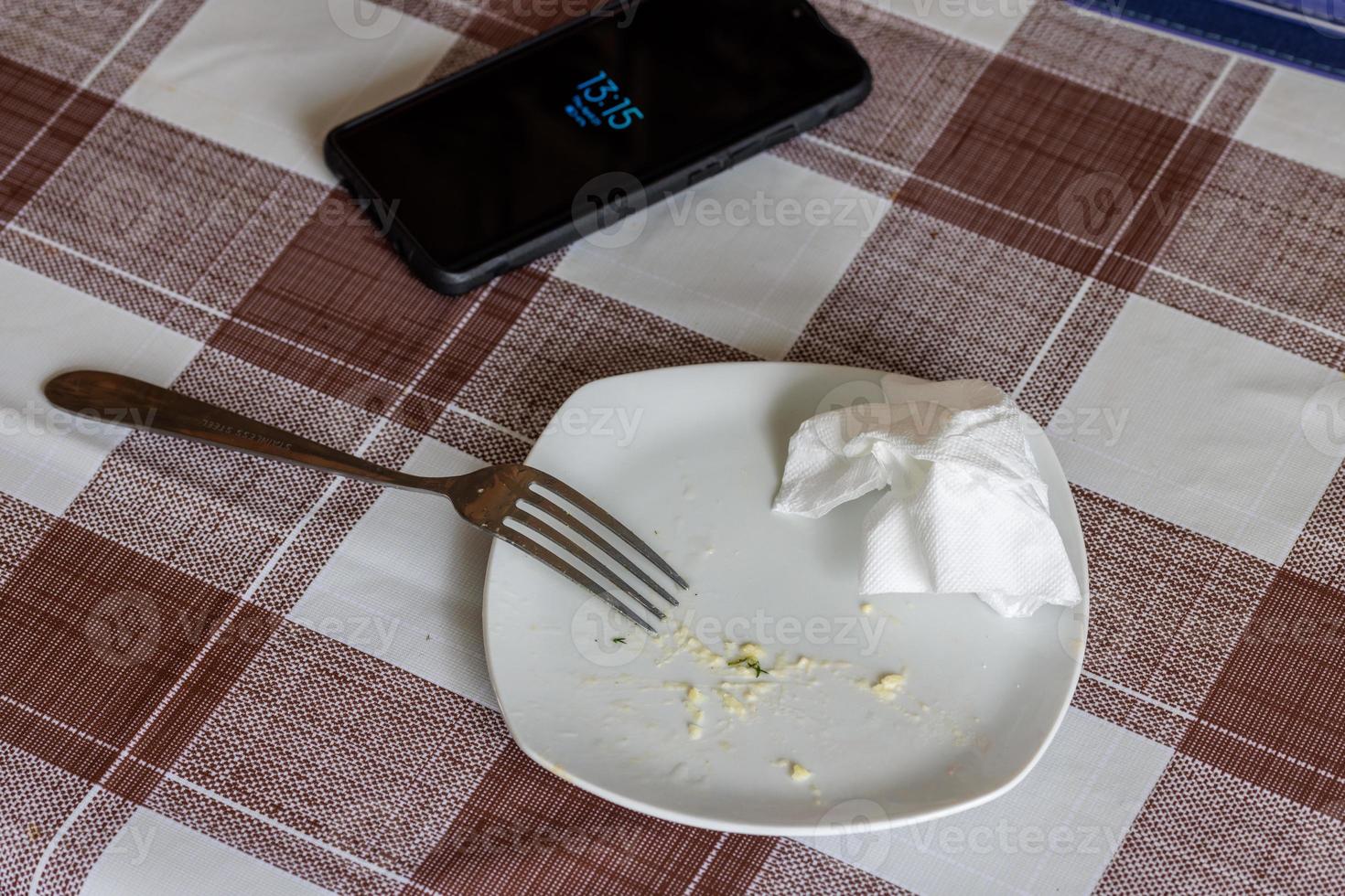 empty white dish with leftovers of eaten food, crumpled table-napkin and steel fork photo