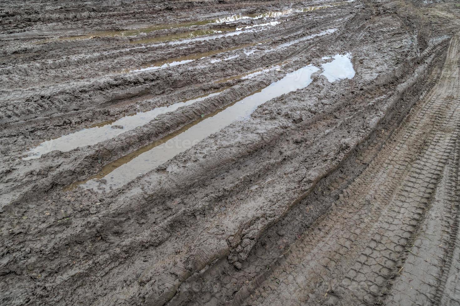 A broken rural country road after the rain. Puddles after rain on a dirt road. Clay, soil and puddles at cloudy day light after rain, autumn season. photo