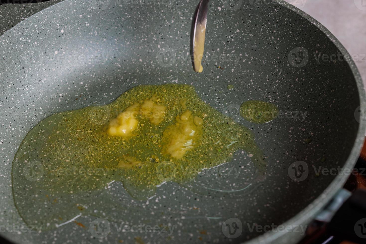 spoon adding butter to vegetable oil on empty preheated skillet photo