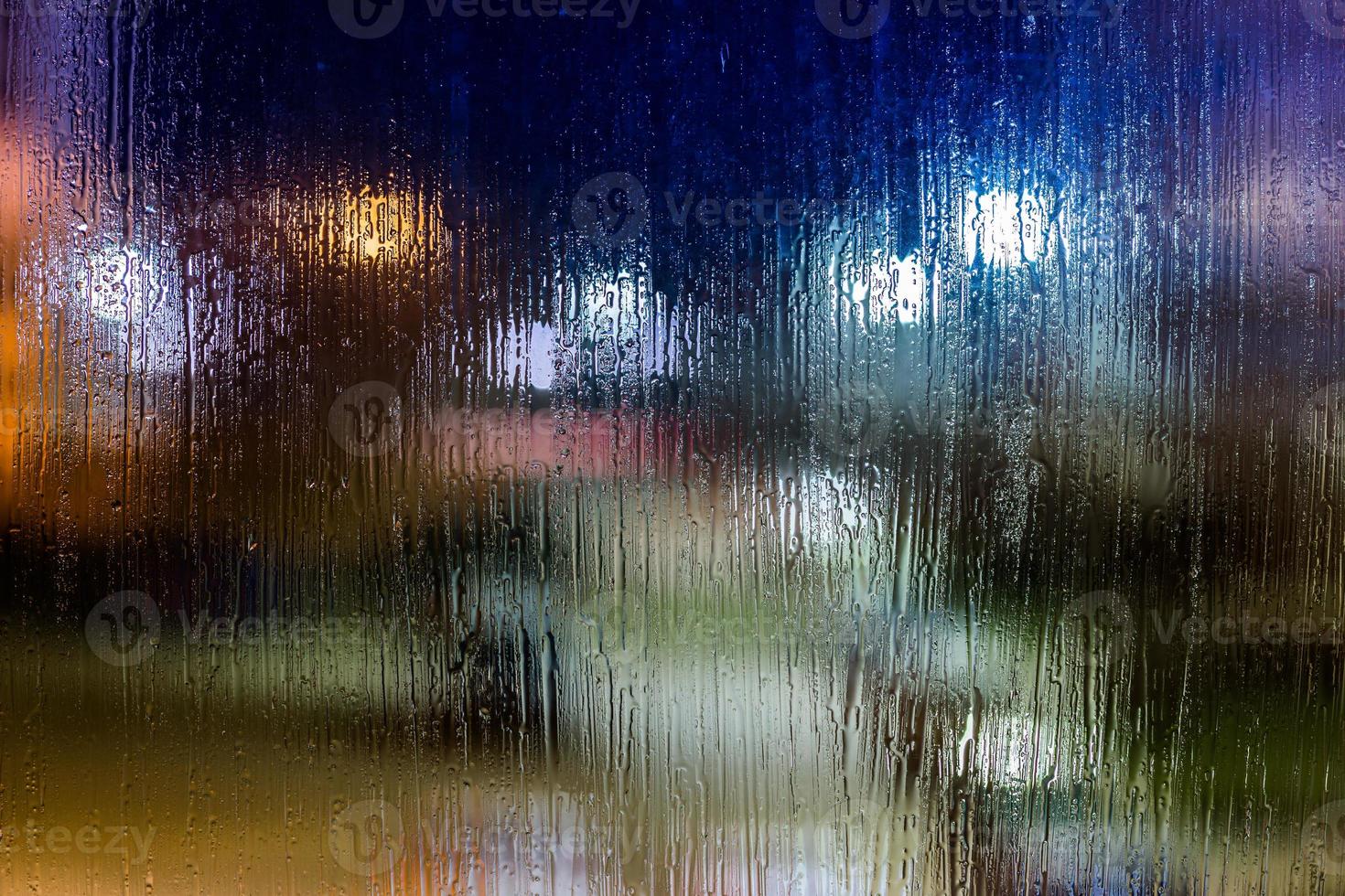 an abstract background night street lights bokeh through wet glass, close-up with selective focus photo