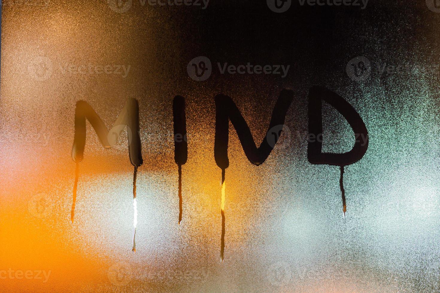 the word mind written on night wet window glass close-up with blurred orange background photo