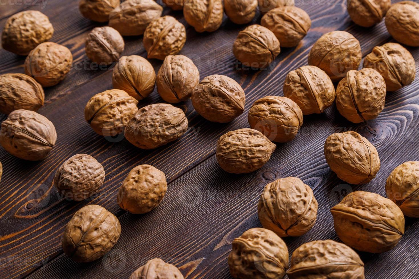 many walnuts with shells randomly scattered on brown wooden surface photo