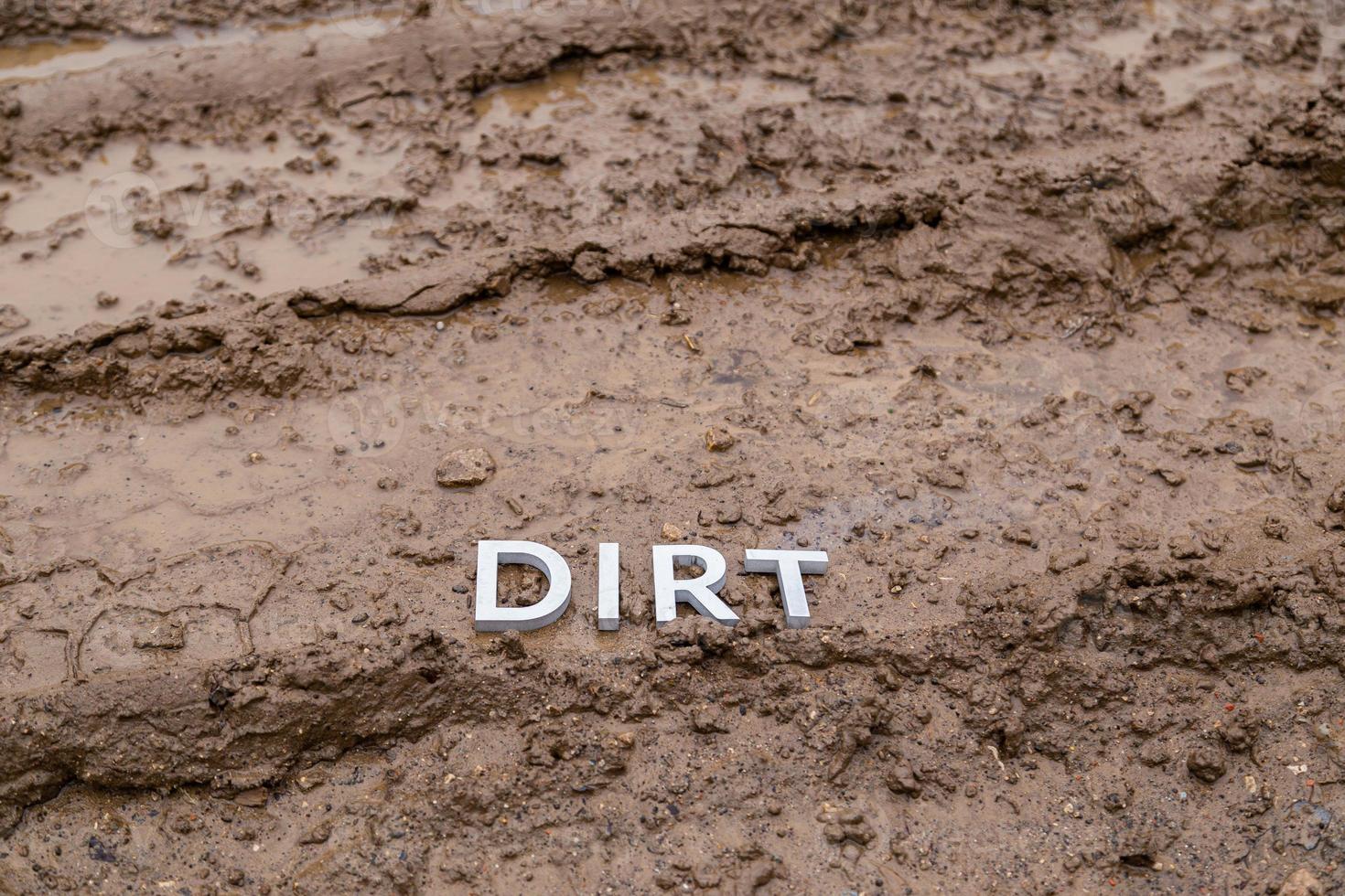 the word dirt laid with silver letters on wet dirt road surface - close-up with selective focus photo