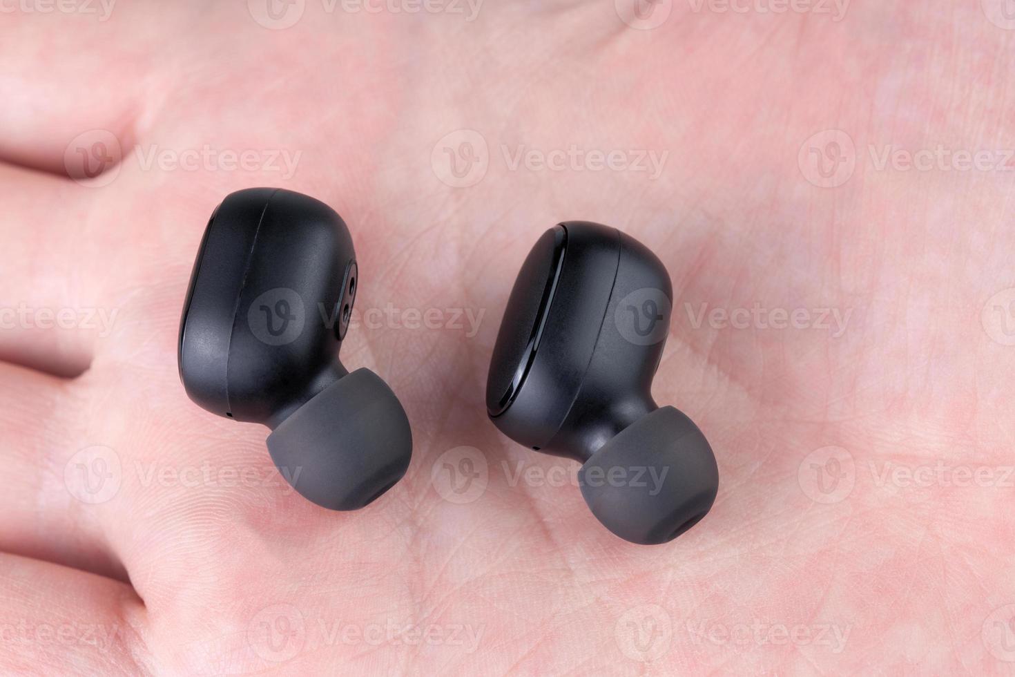 a pair of black wireless earbuds laying on caucasian palm - close-up with selective focus photo