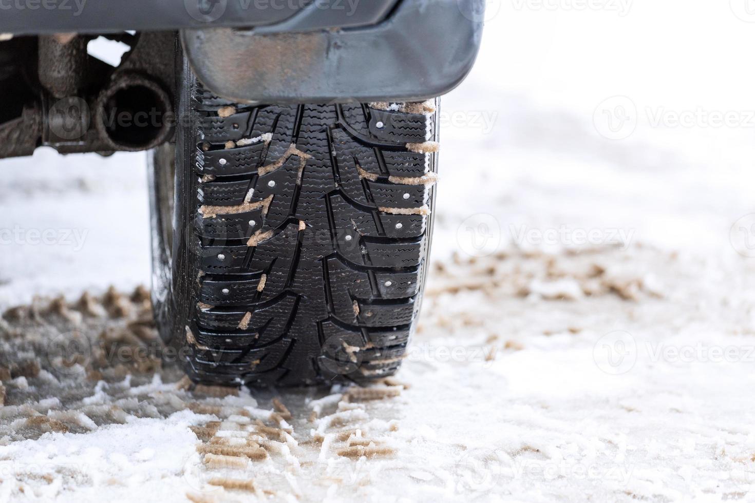 an unadorned picture of winter car wheel with metal spikes on snow close-up photo