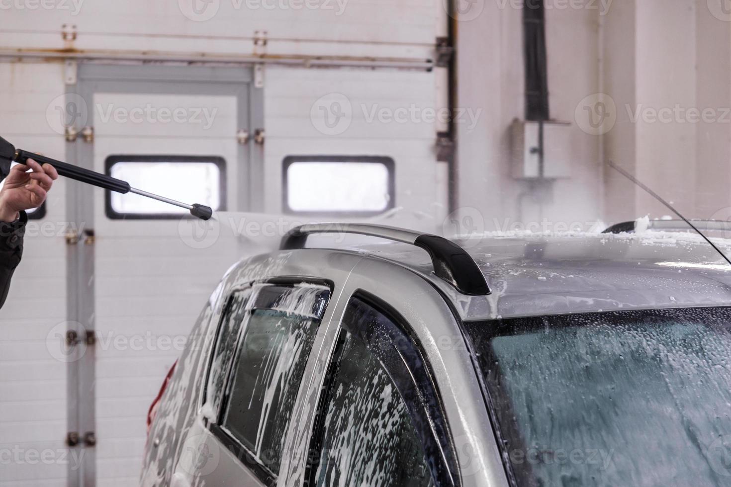 Indoor car washing. Process of removing soap foam from roof of vehicle - close-up vith selective focus. photo