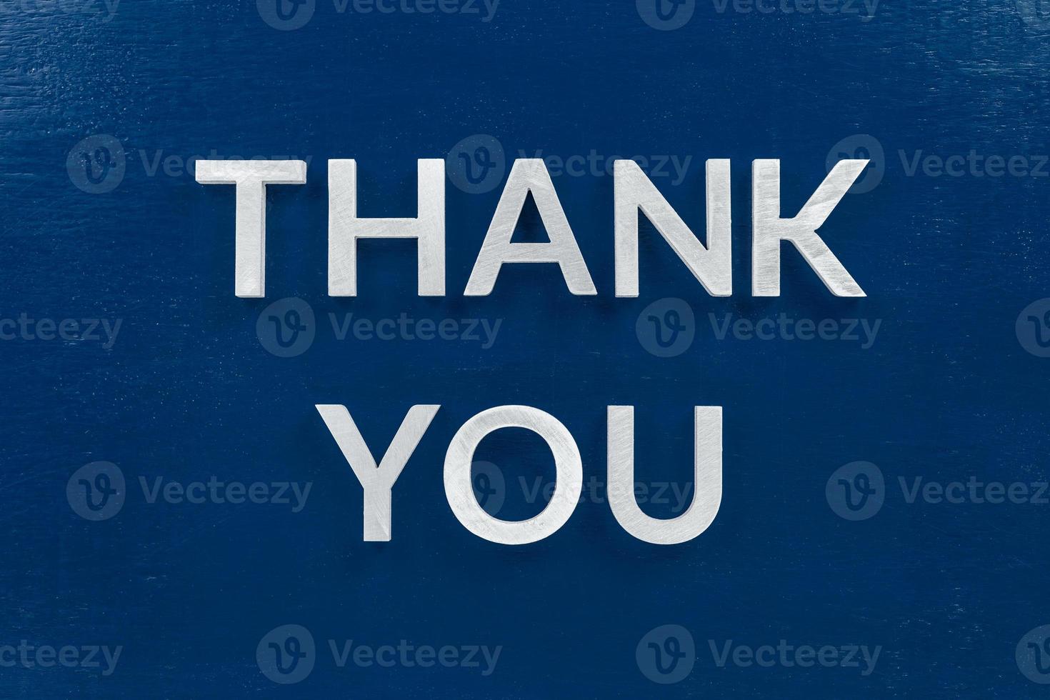 the words thank you laid with aluminium white metal letters on painted flat blue background - directly above in flat lay composition photo