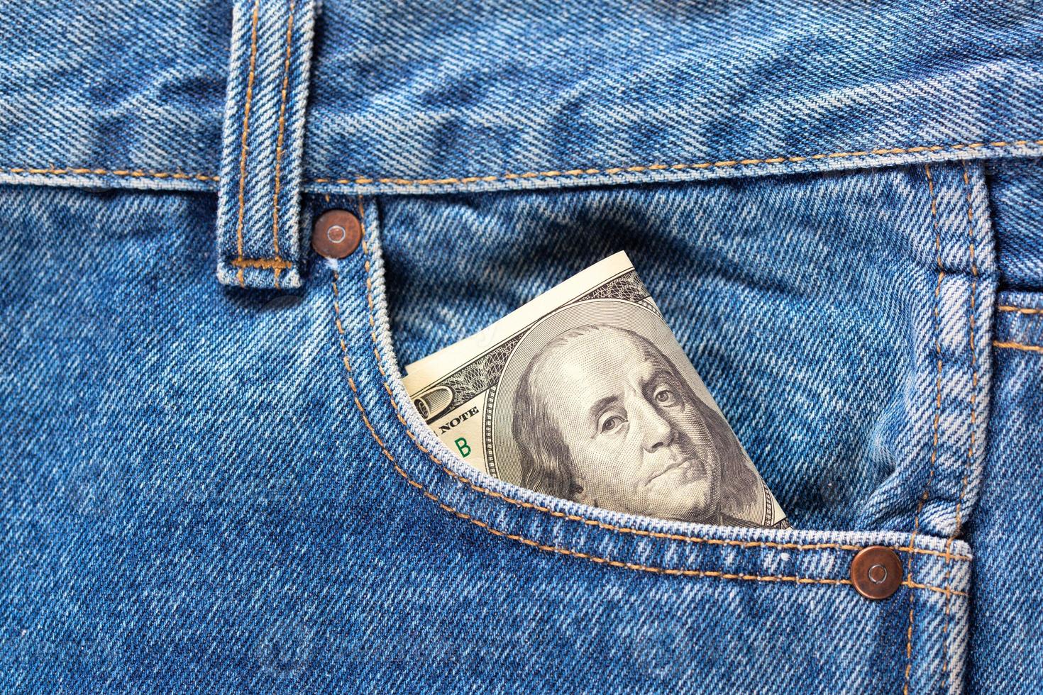 US dollar banknotes in the right front pocket of blue jeans. Concept of saving money or pocket expenses photo