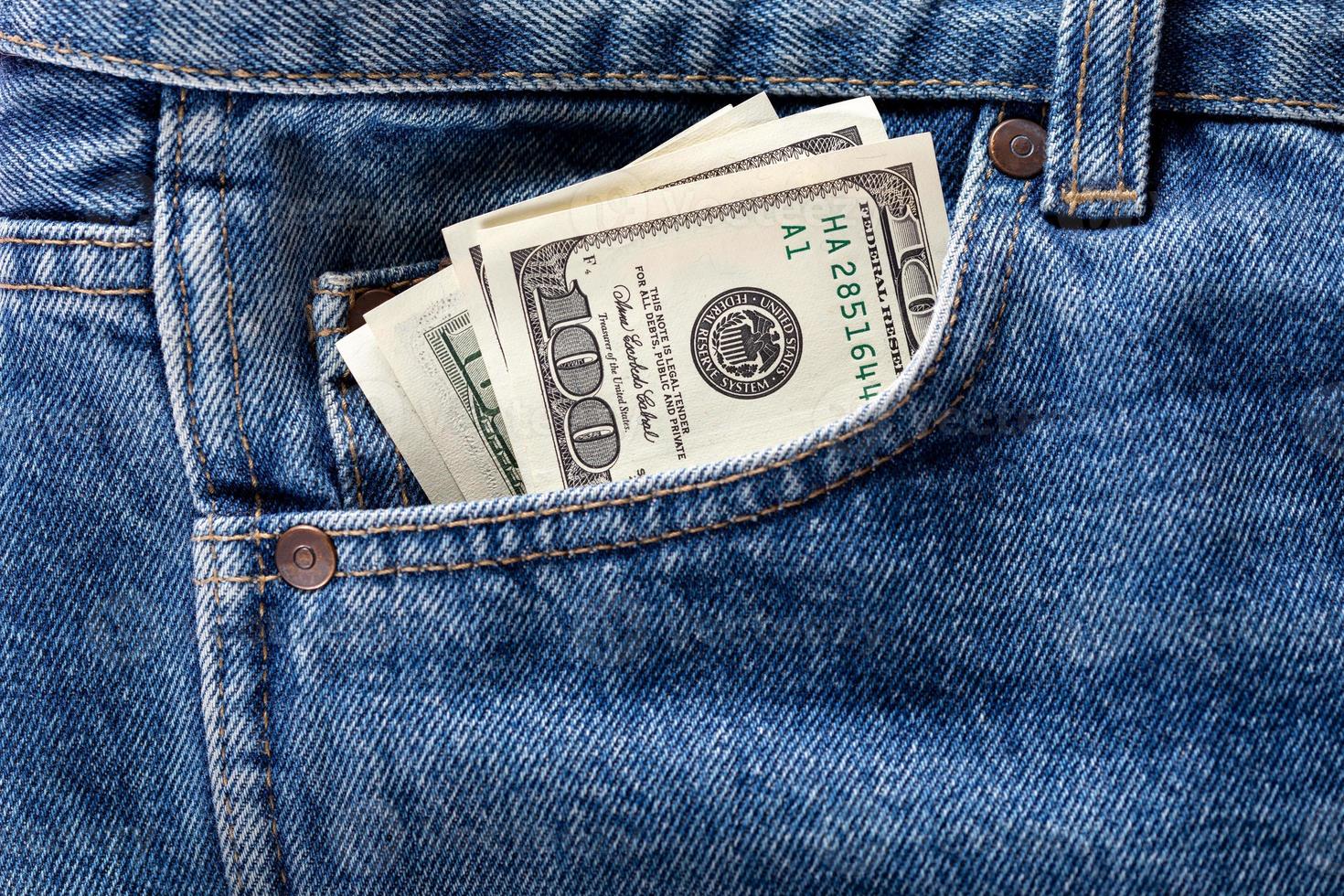 US dollar banknotes in the front left pocket of blue jeans. Concept of saving money or pocket expenses photo