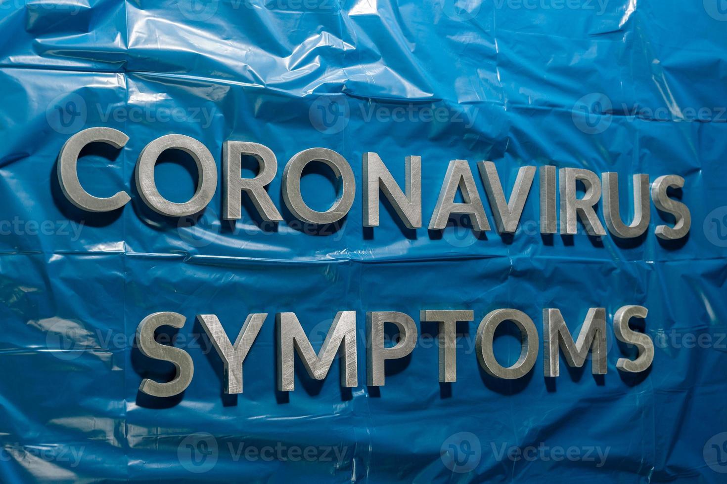 the words coronavirus symptoms laid with silver letters on crumpled blue plastic film - linear perspective composition with selective focus photo