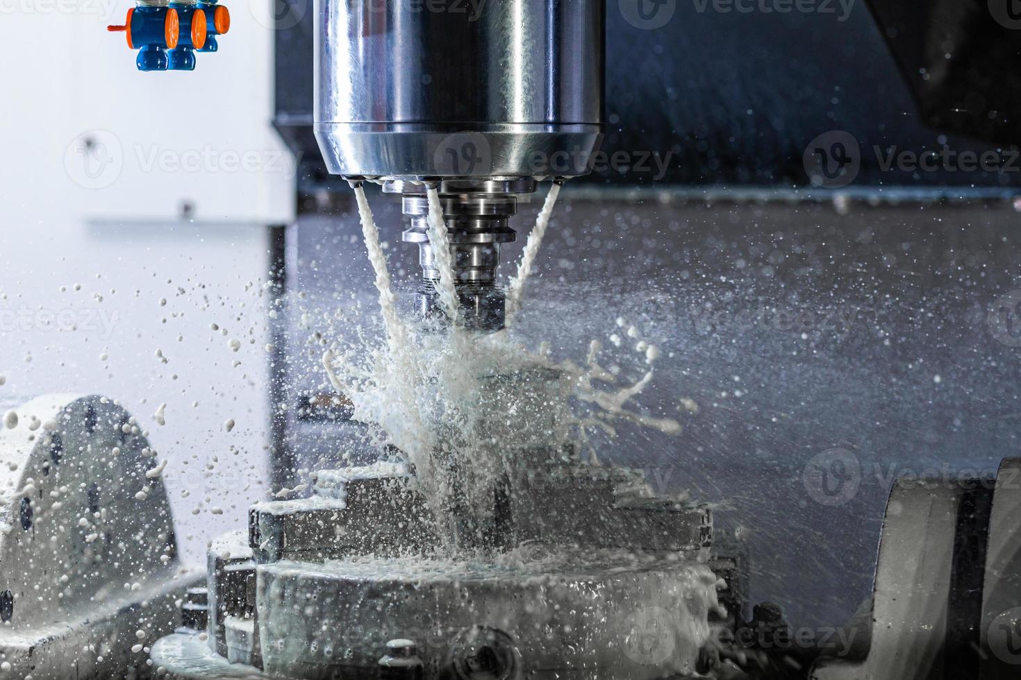 a process of industrial wet milling in 5-axis cnc machine with coolant flow under pressure and freezed splashes photo