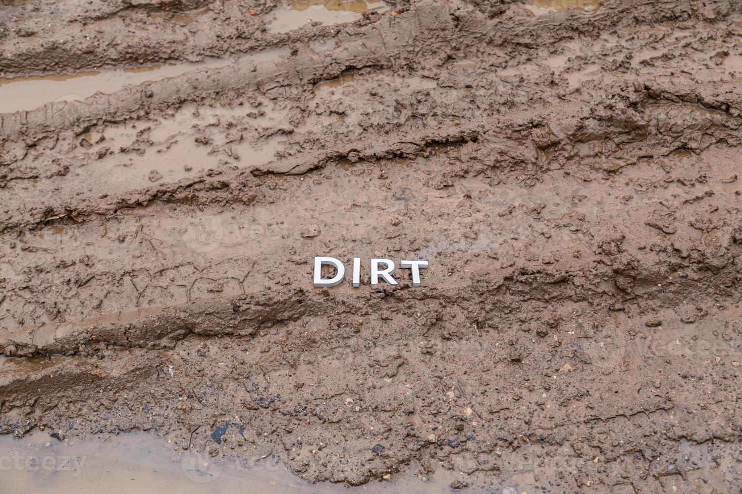 the word dirt laid with silver letters on wet dirt road surface - close-up with selective focus photo