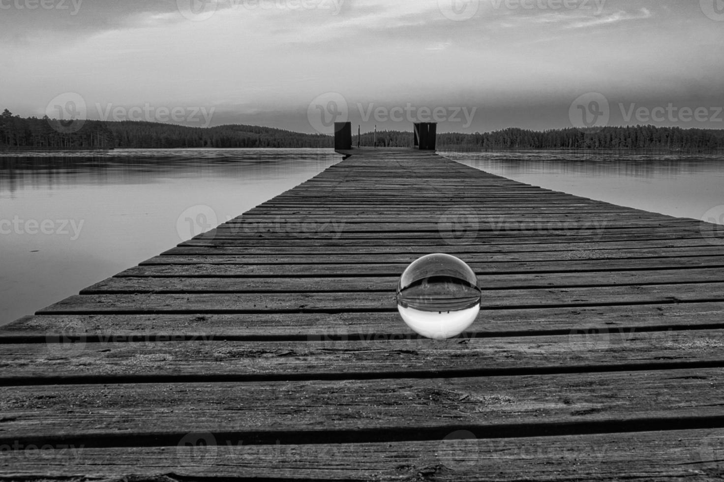 Glass ball on a wooden pier at a Swedish lake at dusk in black and white. Nature photo
