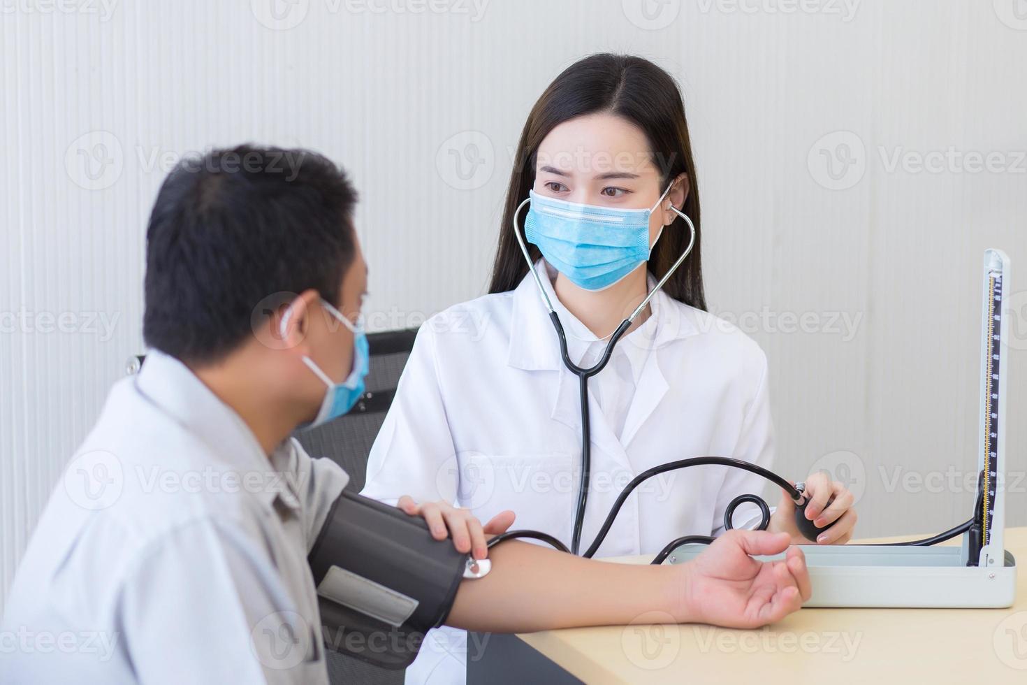 Asian woman doctor listen pulse heart rate by use stethoscope put on foldable joint of a man patient and pump rubber of a blood pressure meter. photo