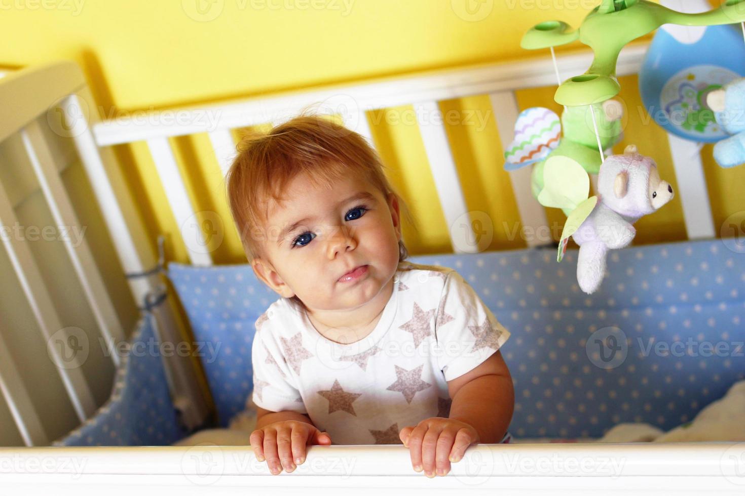 Cute one year old girl with blue eyes and blond hair just woke up in the morning in her bed. photo
