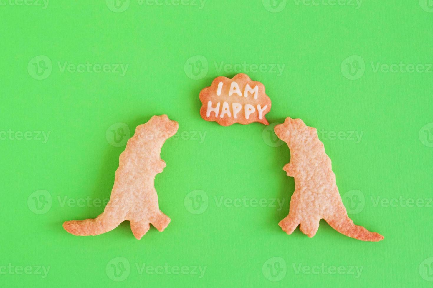 Homemade shortbread cookies in shapes of dinosaurs with callout cloud with text - I am happy - on green background, top view. photo
