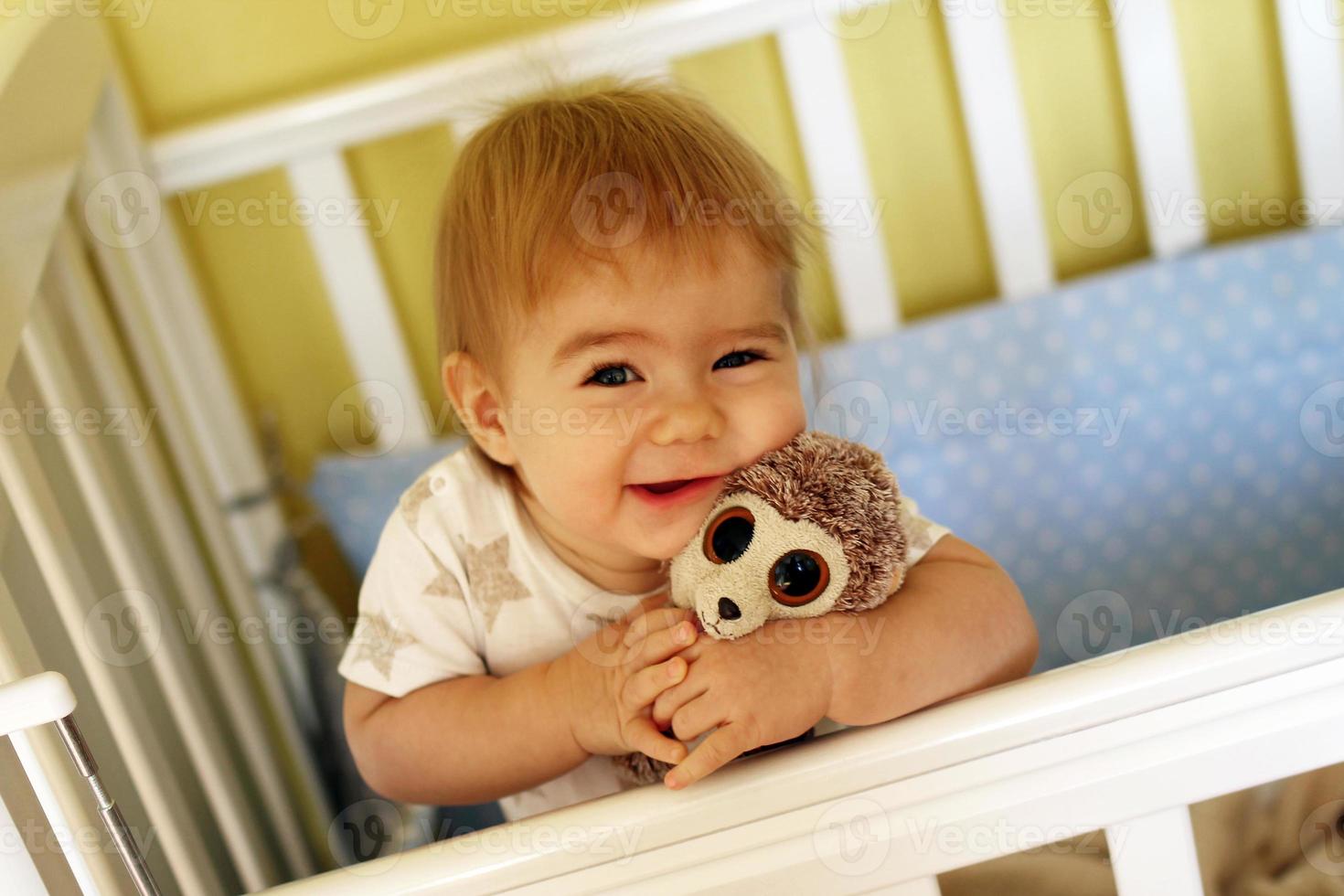 Adorable smiling one year old girl is hugging soft toy after waking up