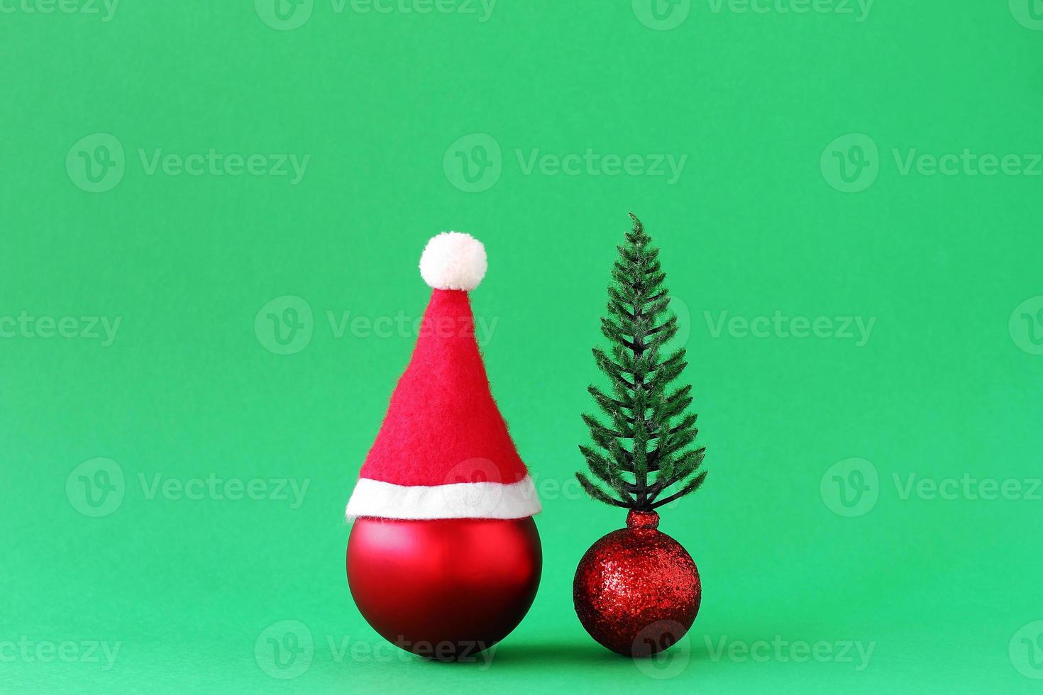 Red Christmas ball with Santa Claus red hat and shiny red ball with artificial Christmas tree on green background with copy space. Minimal Christmas and New Year concept. photo