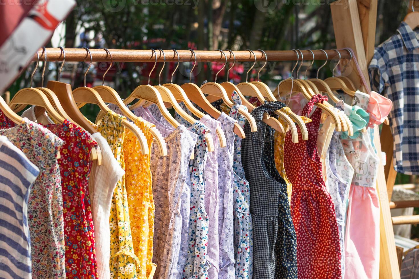 Wooden clothes racks with hangers and with colorful dresses. Showcase with clothes on street market. photo