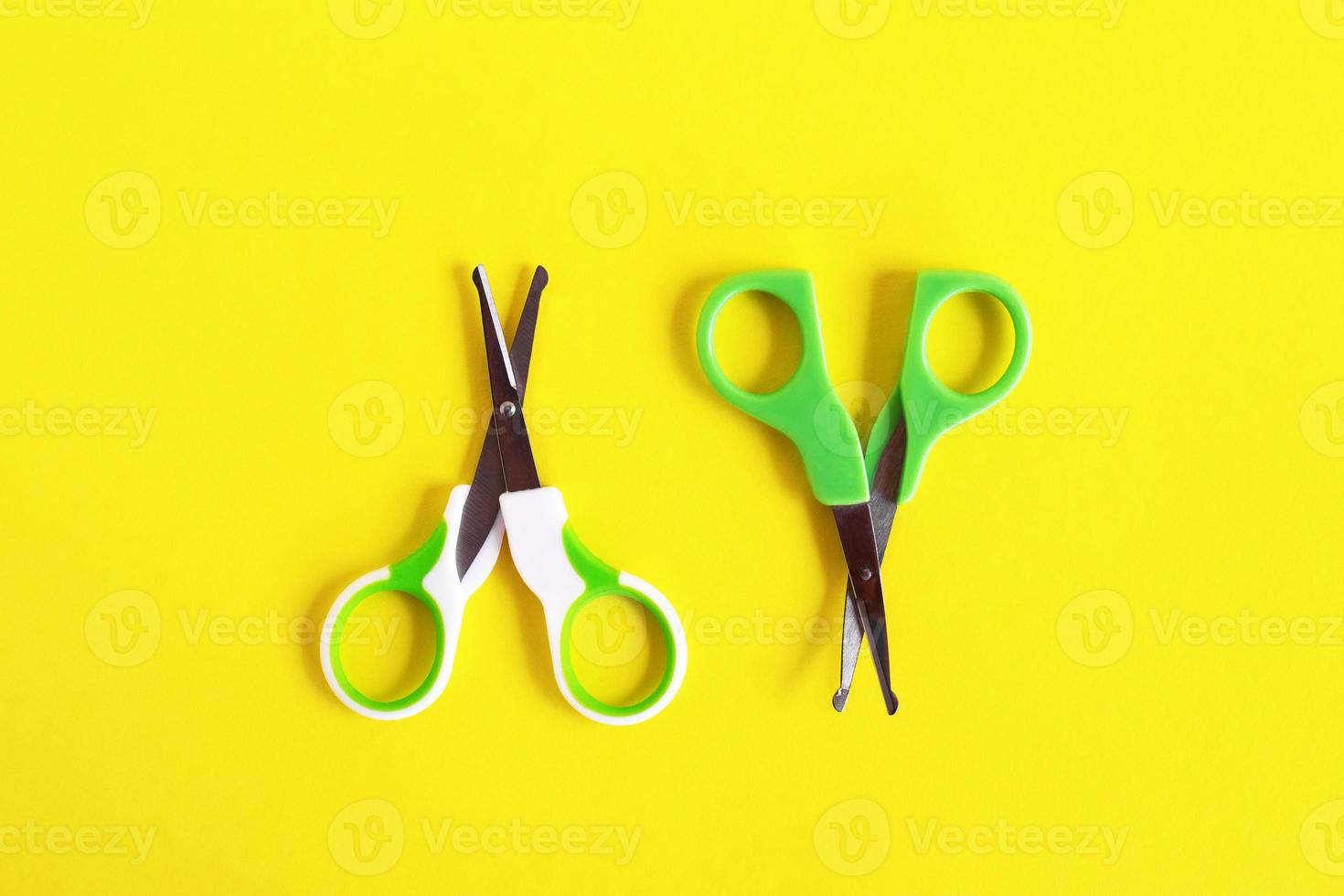 Two open baby green scissors on yellow background, flat lay with copy space. Baby care concept. photo