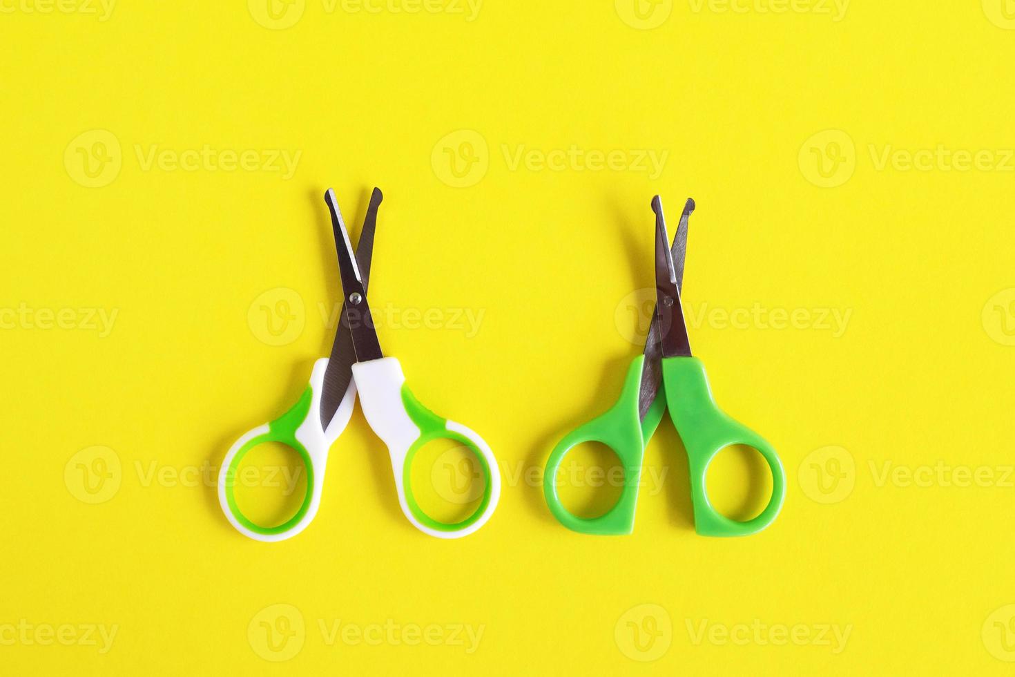 Two open baby green scissors on yellow background, flat lay with copy space. Baby care concept. photo