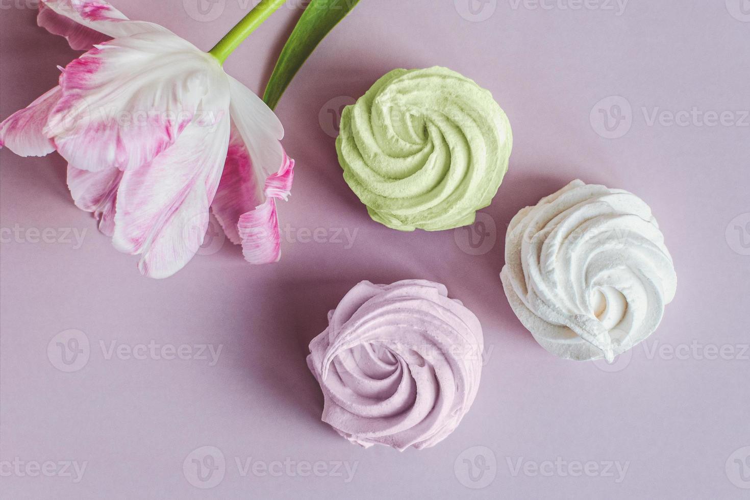 Italian meringue cookies with flower on pink background, spring sweets flat lay photo