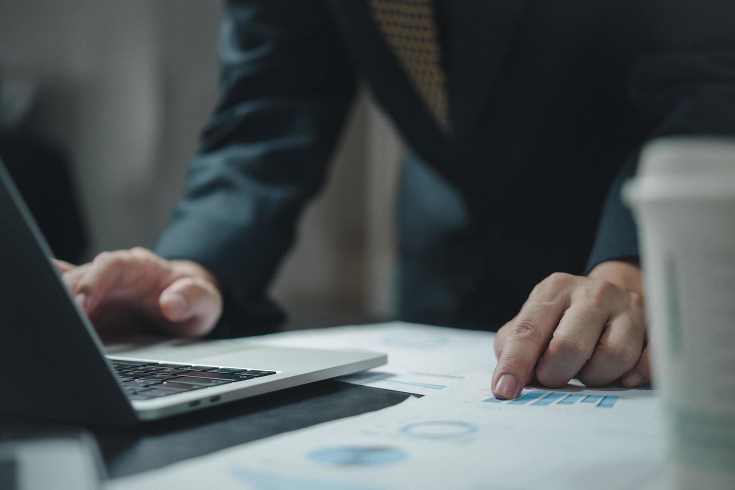 Businessman hand pointing paperwork chart report analysis statistic and document financial graph with computer laptop at office.Business investment marketing on desk in company. photo