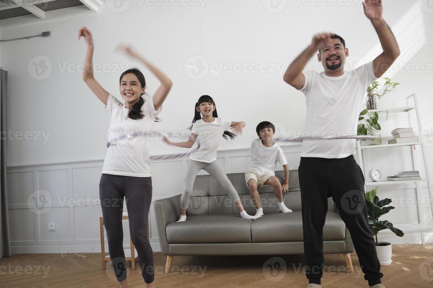 Happy wellness Asian Thai family, parents, and children are fun playing hula hoops together, fitness training and healthy exercise in white living room, domestic home lifestyle, and weekend activity. photo