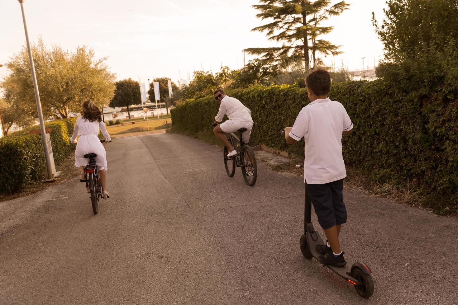 familia feliz disfrutando de una hermosa mañana juntos, padres montando en bicicleta y su hijo montando un scooter eléctrico. enfoque selectivo foto