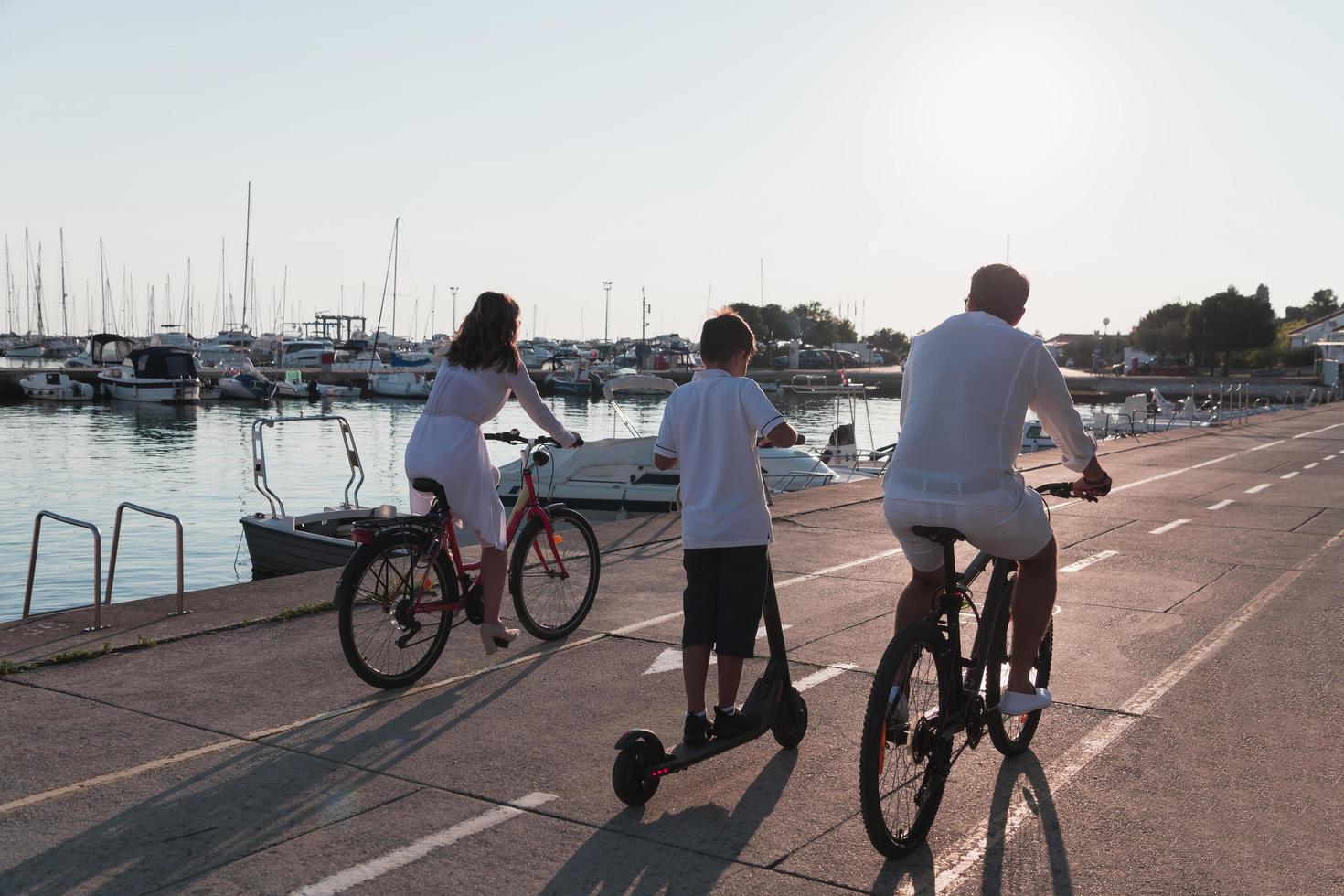Happy family enjoying a beautiful morning by the sea together, parents riding a bike and their son riding an electric scooter. Selective focus photo