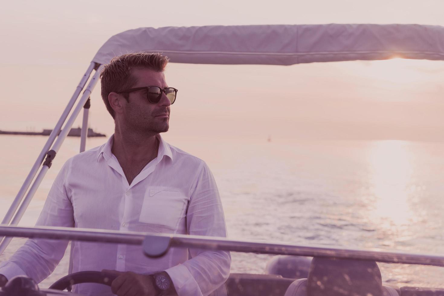 A determined senior businessman in casual clothes and sunglasses enjoys his vacation driving a luxury boat at sunset. Selective focus photo
