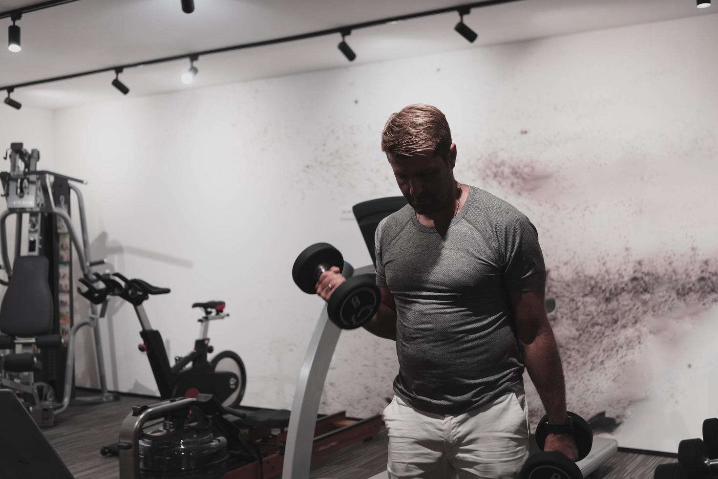 Struggling with age. Confident senior man exercising with dumbbells in health club. Selective focus photo